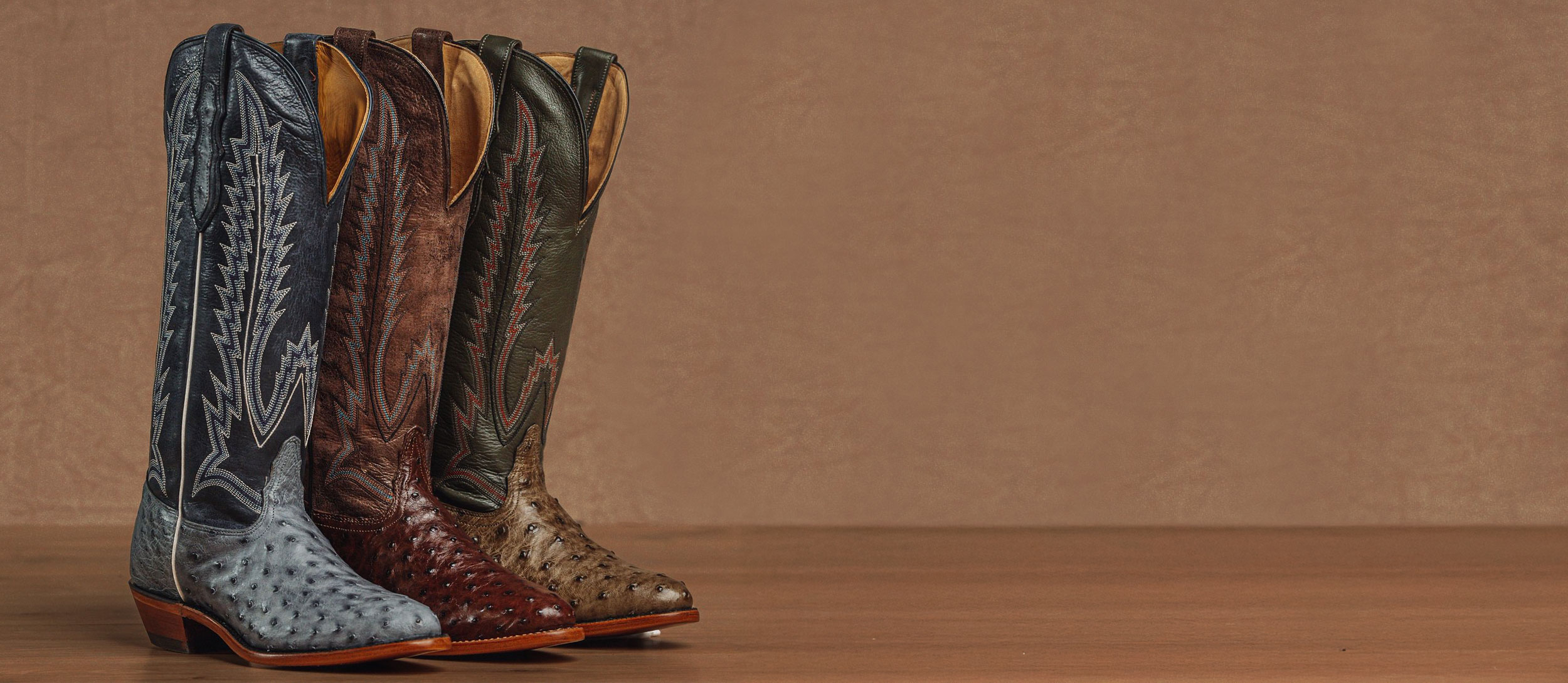 A lineup of the Quintana 15” Full Quill Ostrich Boot in front of a wood wall.